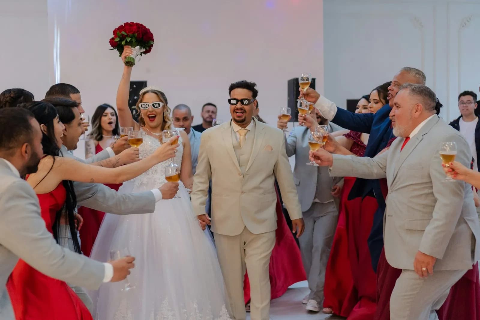 A bride and groom walking into their reception while guests on both sides raise their glasses, the bride holding her bouquet high.