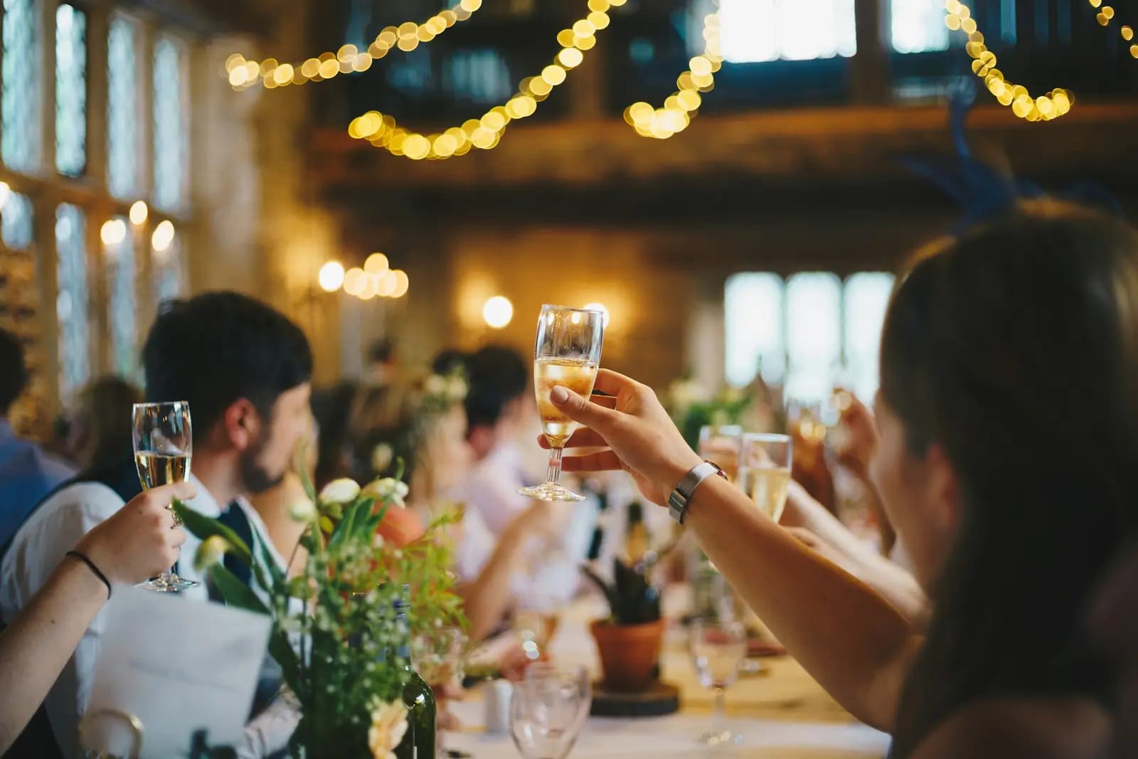 A raised glass at a long table under warm string lights.